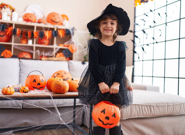 Adorable chica hispana teniendo fiesta de halloween sosteniendo canasta de calabaza en casa - Foto, Imagen