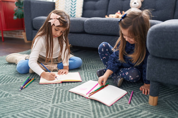 Чарівні дівчата студенти сидять на підлозі малюють на блокноті вдома
 - Фото, зображення