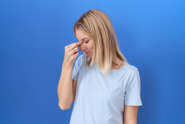 Молода біла жінка в повсякденній блакитній сорочці втомилася розтирати ніс і очі, відчуваючи втому і головний біль. концепція стресу та розчарування.  - Фото, зображення