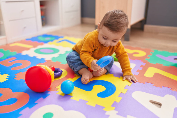Adorable caucasian baby playing with hoops sitting on floor at kindergarten - Foto, Bild
