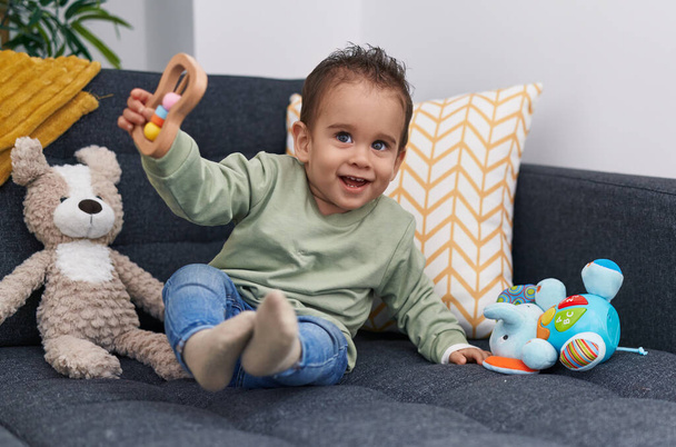 Evdeki kanepede oturan sevimli İspanyol çocuk oyuncakla oynuyor. - Fotoğraf, Görsel