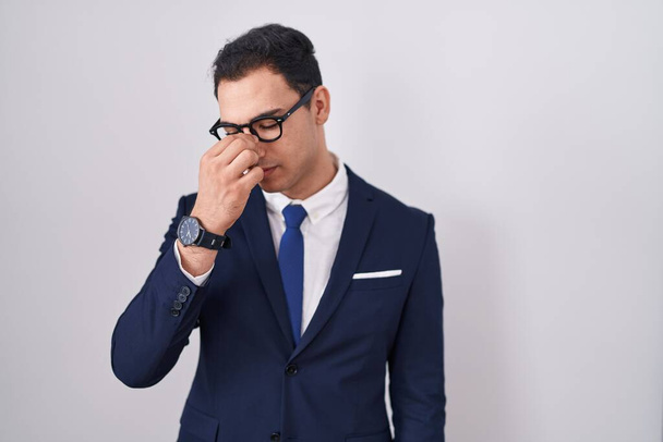 Young hispanic man wearing suit and tie tired rubbing nose and eyes feeling fatigue and headache. stress and frustration concept.  - Foto, afbeelding