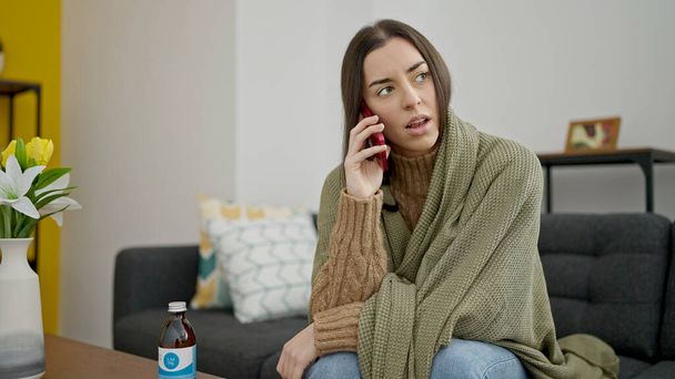 Jeune belle femme hispanique couvrant avec couverture pour parler froid sur smartphone à la maison - Photo, image