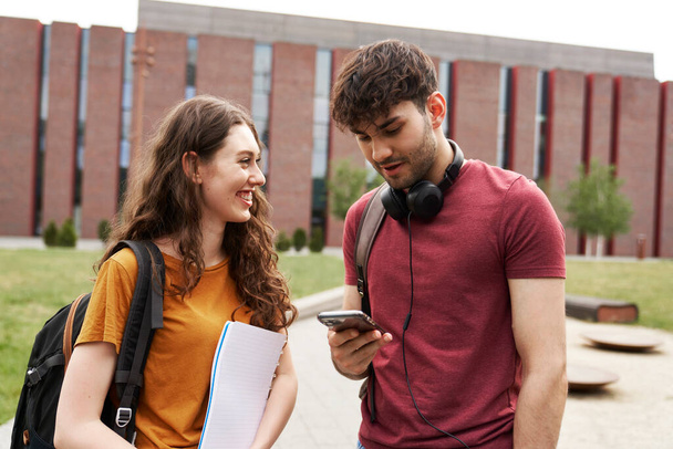 Two students browsing phone next to to university campus - Valokuva, kuva