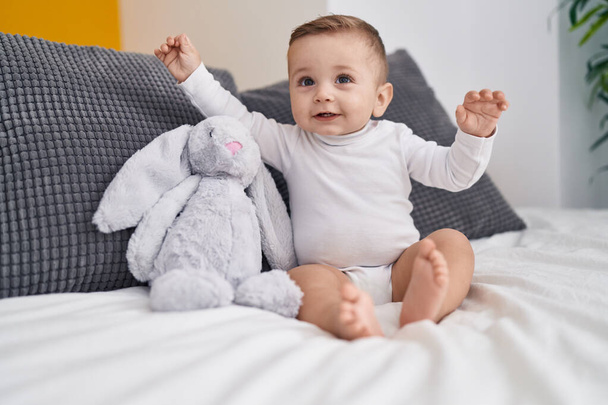Schattige blanke baby glimlachend zelfverzekerd zittend op bed in de slaapkamer - Foto, afbeelding
