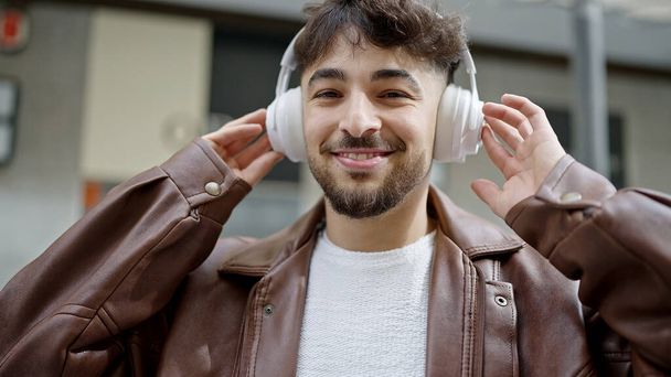 Fiatal arab férfi mosolyog magabiztos zenét hallgat az utcán - Fotó, kép