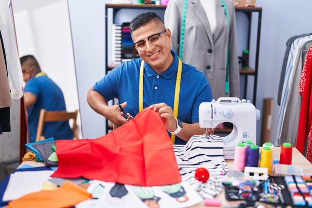 Young latin man tailor smiling confident cutting cloth at atelier - Fotoğraf, Görsel