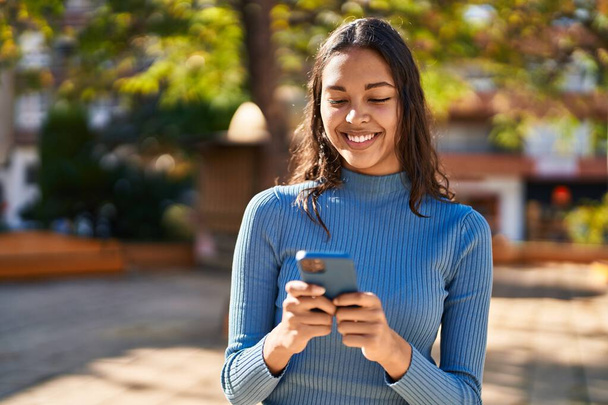 Jeune femme afro-américaine souriante confiante en utilisant un smartphone au parc - Photo, image