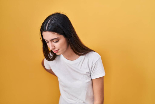 Young beautiful woman standing over yellow background suffering of backache, touching back with hand, muscular pain  - Photo, Image