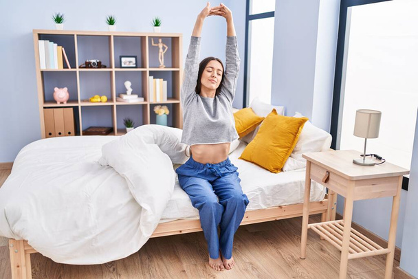 Young beautiful hispanic woman waking up stretching arms at bedroom - Photo, Image