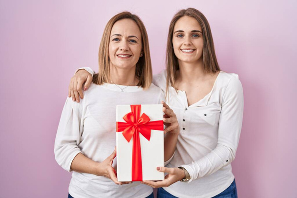 Middle age mother and young daughter holding mothers day gift smiling with a happy and cool smile on face. showing teeth.  - 写真・画像