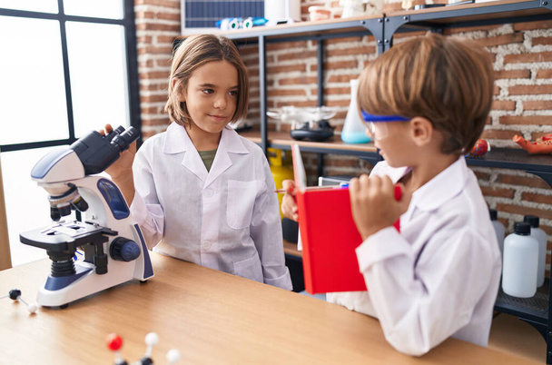 Entzückende Jungenschüler schreiben im Labor Notizen unter dem Mikroskop - Foto, Bild