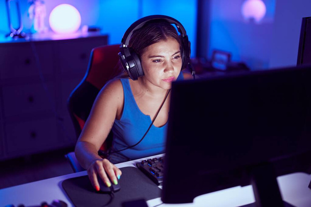 Young beautiful hispanic woman streamer playing video game using computer at gaming room - Foto, imagen