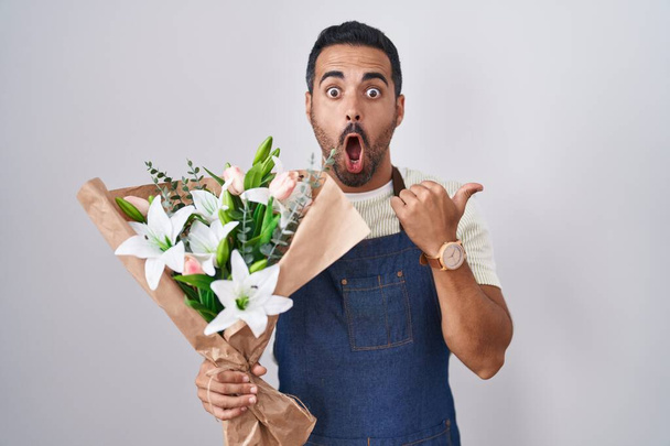 Spanyol férfi szakállas dolgozik, mint virágárus meglepett mutató kéz ujját oldalra, nyitott száj elképedt kifejezés.  - Fotó, kép