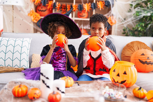 Adorable afroamericano chico y chica teniendo halloween fiesta inflando globo en casa - Foto, imagen