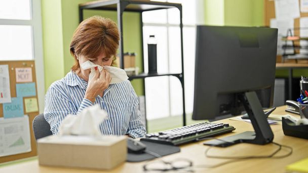 Geschäftsfrau mittleren Alters niest im Büro am Computer - Foto, Bild