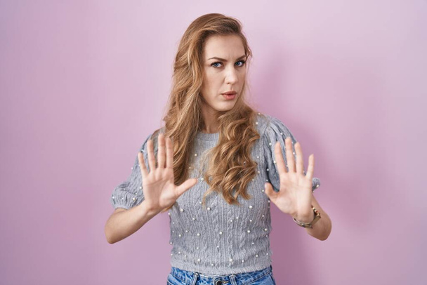 Beautiful blonde woman standing over pink background moving away hands palms showing refusal and denial with afraid and disgusting expression. stop and forbidden.  - Photo, Image