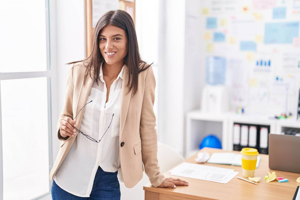 Junge schöne hispanische Geschäftsfrau lächelt selbstbewusst im Büro - Foto, Bild