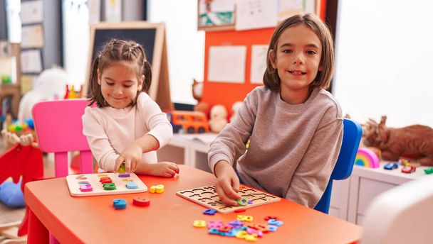 Adorable boy and girl playing with maths puzzle game sitting on table at kindergarten - Photo, Image