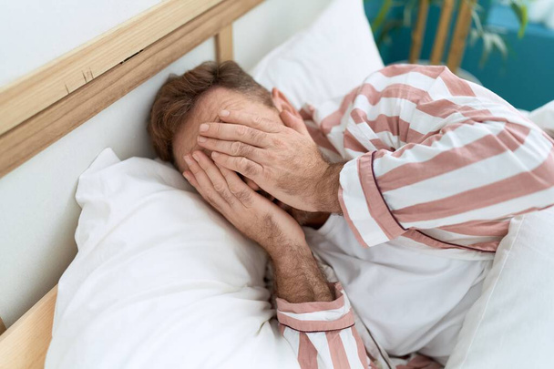 Middelbare leeftijd man gestrest liggend op bed in de slaapkamer - Foto, afbeelding