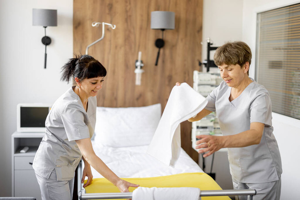 As empregadas fazem a cama na enfermaria. Conceito de condições confortáveis e modernas para a permanência médica dos pacientes - Foto, Imagem