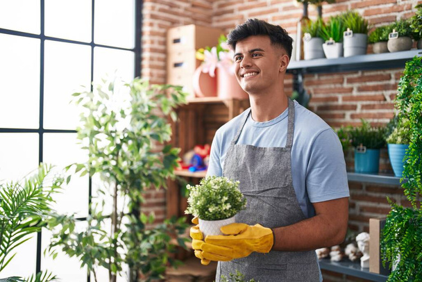 Jeune homme hispanique fleuriste souriant confiant tenant plante à la boutique de fleurs - Photo, image