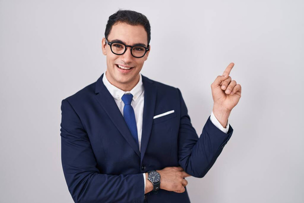Young hispanic man wearing suit and tie with a big smile on face, pointing with hand and finger to the side looking at the camera.  - Фото, изображение