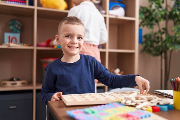 Adorable caucasian boy playing with puzzle game sitting on table at kindergarten - Фото, изображение
