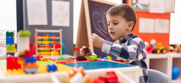 Schattige blanke jongen spelen met bouwstenen zitten op tafel op de kleuterschool - Foto, afbeelding