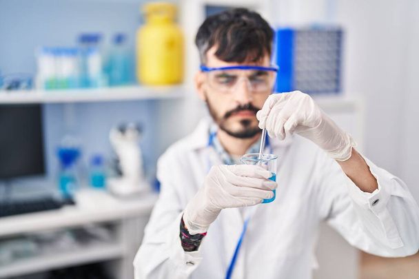 Científico joven hispano mezclando líquido sobre vidrio en laboratorio - Foto, Imagen