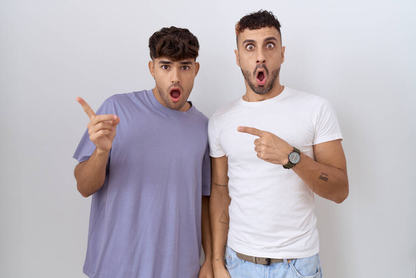 homosexuel gay couple debout sur blanc fond surpris pointant avec doigt sur l 'côté ouvert bouche amazed expression.  - Photo, image
