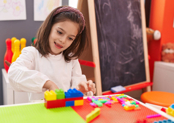 Adorable hispanic girl playing with construction blocks sitting on table at kindergarten - Photo, image