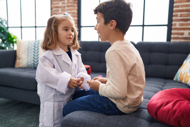Adorable niño y niña vistiendo uniforme médico hablando en casa - Foto, imagen