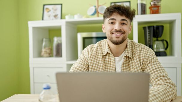 Young arab man using laptop sitting on table at home - Photo, Image