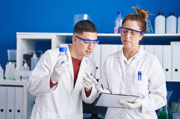 Man and woman scientists write on document holding bottle at laboratory - Φωτογραφία, εικόνα