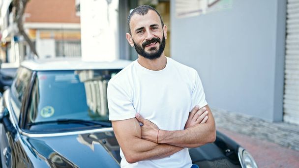 Young hispanic man smiling confident sitting on car with arms crossed gesture at street - Photo, Image