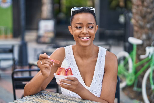 African american woman eating ice cream sitting on table at coffee shop terrace - Photo, Image