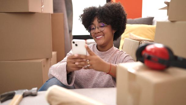 Молода афроамериканська жінка, яка впевнено посміхається, користуючись смартфоном у себе вдома. - Фото, зображення