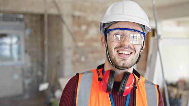 Jonge Spaanse man bouwer glimlachend zelfverzekerd staande op de bouwplaats - Foto, afbeelding