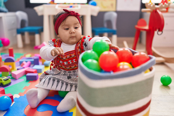 Adorable bebé hispano jugando con bolas sentadas en el suelo en el jardín de infantes - Foto, imagen