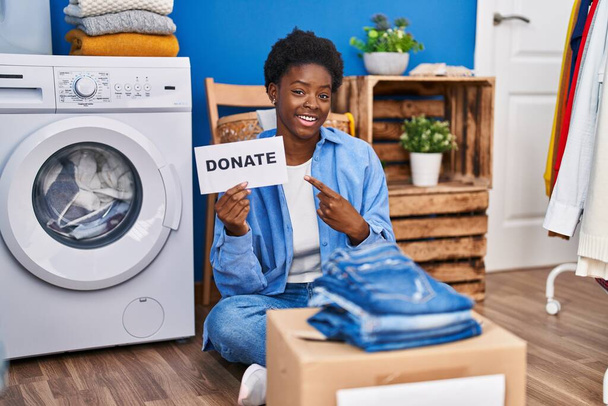 Африканська американка дарує одяг усміхнений щасливий вказуючи рукою і пальцем  - Фото, зображення