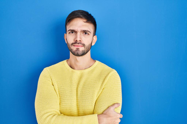 Hispanic man standing over blue background skeptic and nervous, disapproving expression on face with crossed arms. negative person.  - Valokuva, kuva
