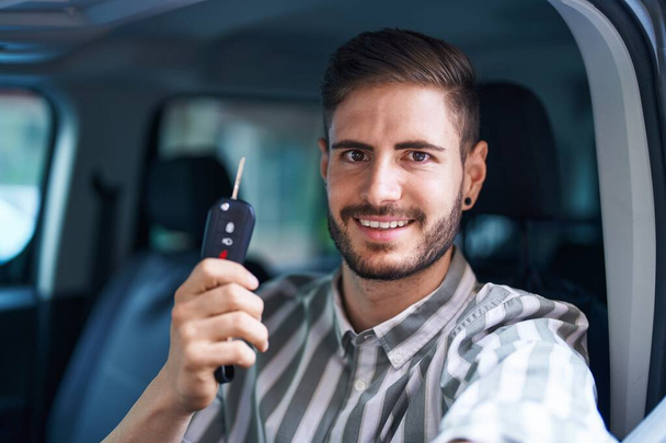 Νεαρός καυκάσιος άνδρας χαμογελά αυτοπεποίθηση κρατώντας το κλειδί του νέου αυτοκινήτου στο δρόμο - Φωτογραφία, εικόνα