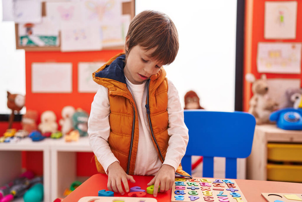 Adorable garçon caucasien jouer avec des mathématiques jeu de puzzle assis sur la table à la maternelle - Photo, image