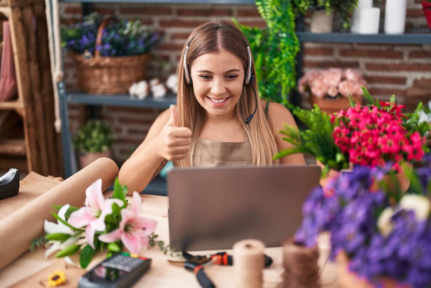 Young blonde woman working at florist shop doing video call smiling happy and positive, thumb up doing excellent and approval sign  - Foto, afbeelding