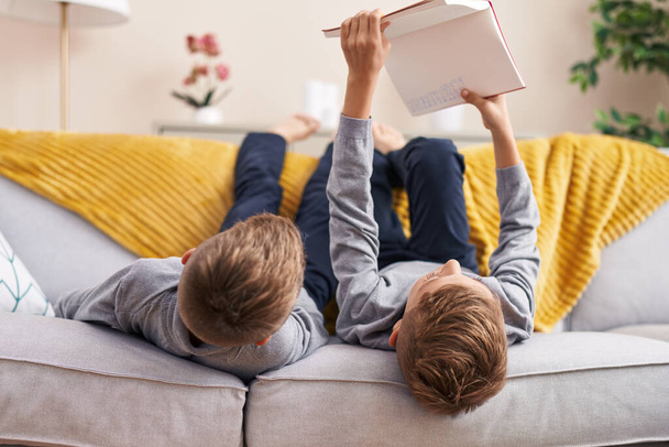 Adorable boys reading book lying on sofa at home - Photo, Image