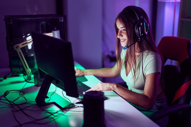 Young beautiful hispanic woman streamer playing video game using computer at gaming room - Photo, Image