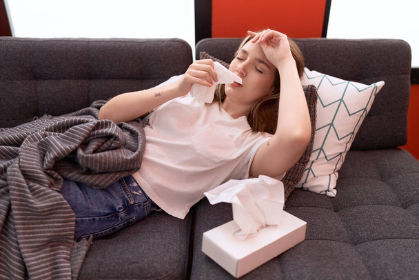 Joven mujer caucásica acostada en el sofá enfermedad usando servilleta en casa - Foto, imagen