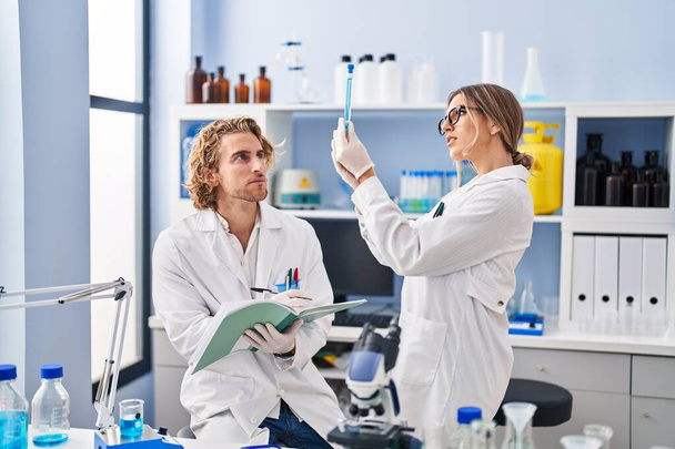 Мужчина и женщина, одетые в форму ученого, держат пробирку на тетради в лаборатории - Фото, изображение