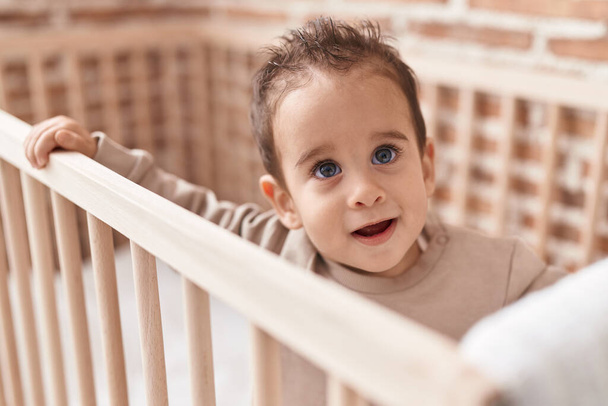 Adorable hispanic boy smiling confident standing on cradle at bedroom - 写真・画像